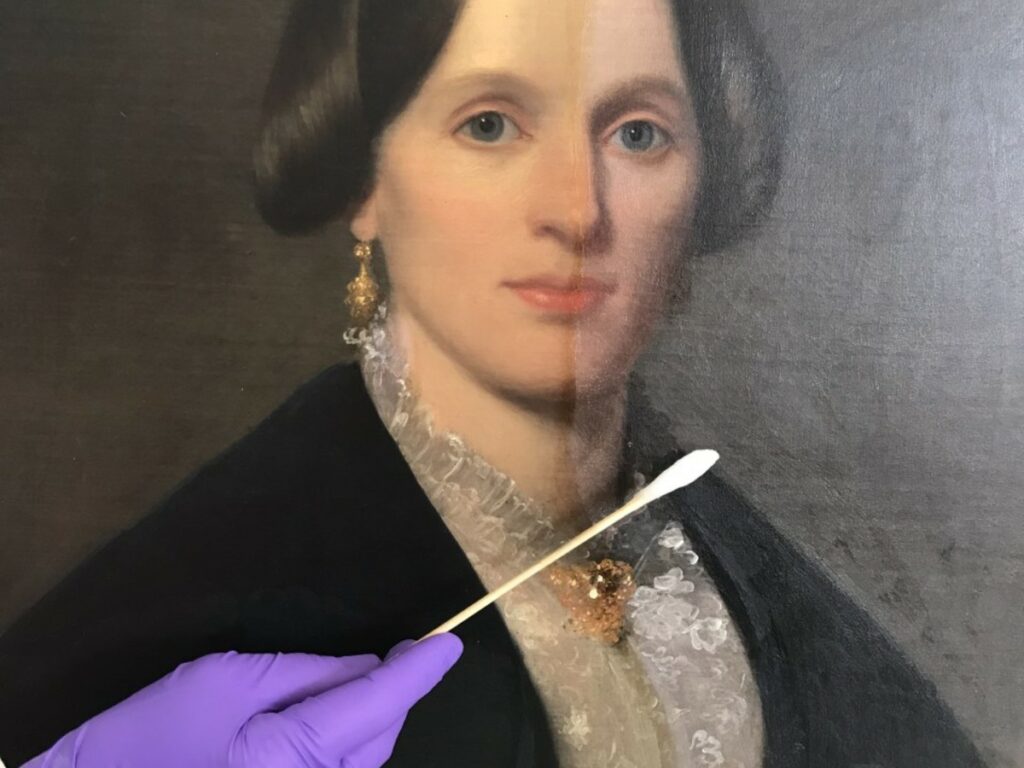 During treatment photograph shows a partially-removed, discolored varnish layer on a painted portrait